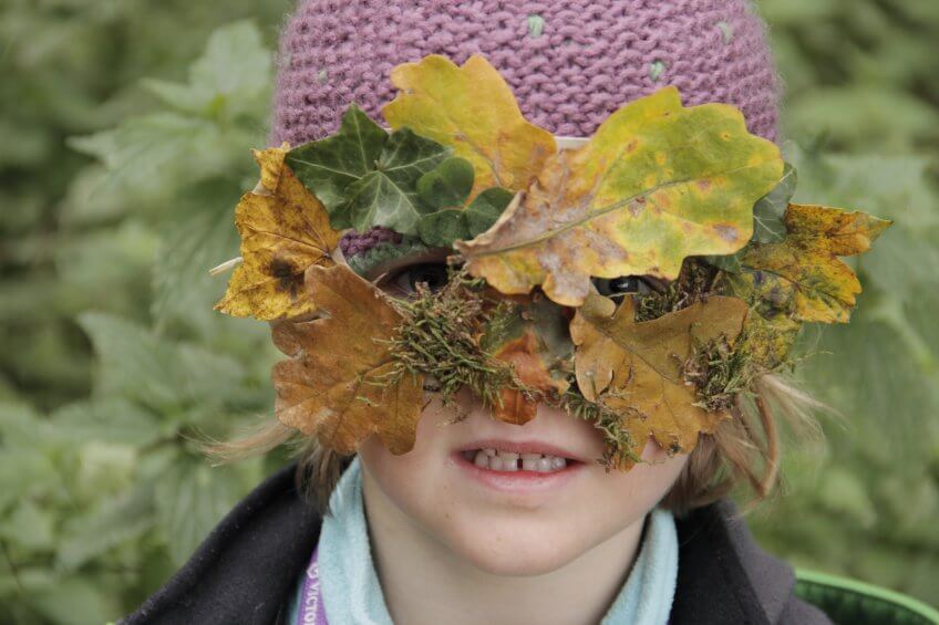 Une enfant avec masque en feuilles.